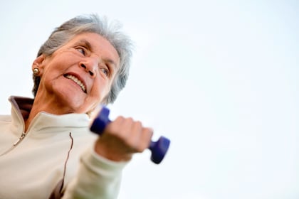 Elder woman exercising outdoors with free-weights and smiling